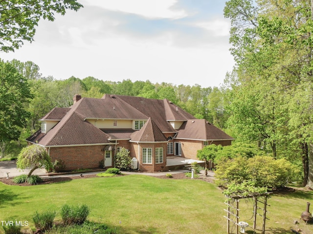 exterior space featuring a shingled roof, a chimney, a yard, and brick siding