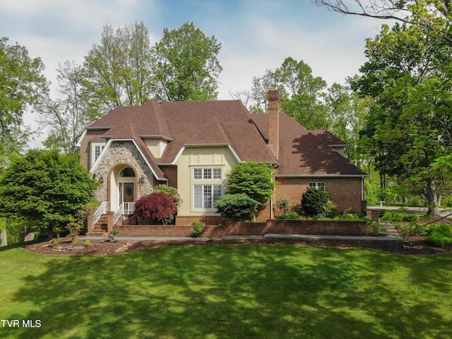 tudor home featuring brick siding, a chimney, stone siding, and a front lawn