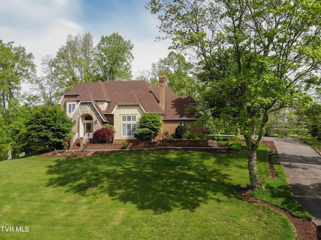 cape cod-style house with a chimney, roof with shingles, stone siding, and a front yard