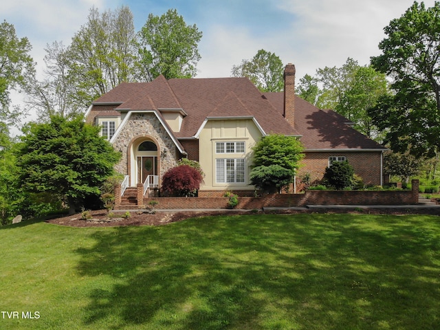 tudor home with brick siding, a chimney, stone siding, and a front lawn