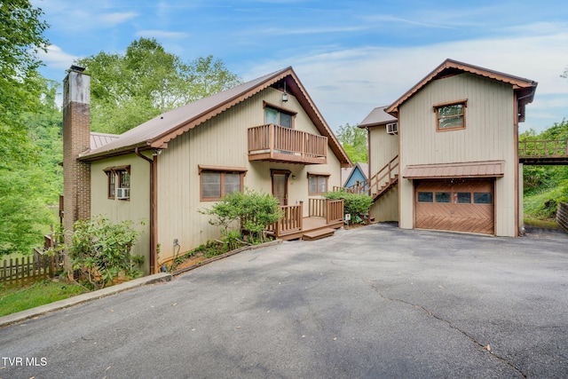 chalet / cabin with a balcony, a chimney, fence, metal roof, and aphalt driveway