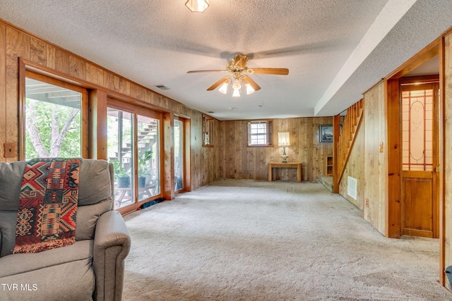 living area with wooden walls, visible vents, ceiling fan, and light carpet