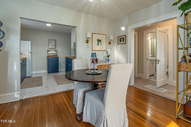 dining room with a textured ceiling, baseboards, and light wood-type flooring