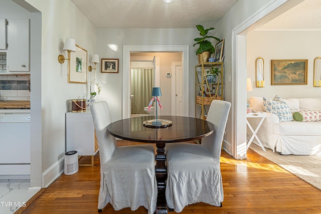 dining room with light wood-type flooring, a textured ceiling, and baseboards