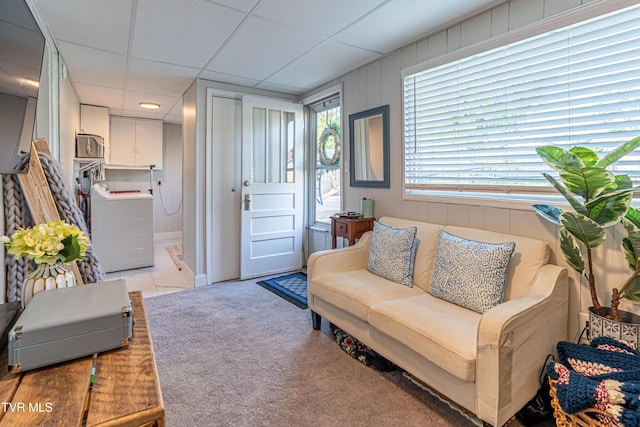 living room featuring washer / clothes dryer, a drop ceiling, and light carpet