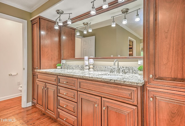 bathroom with double vanity, wood finished floors, a sink, crown molding, and baseboards