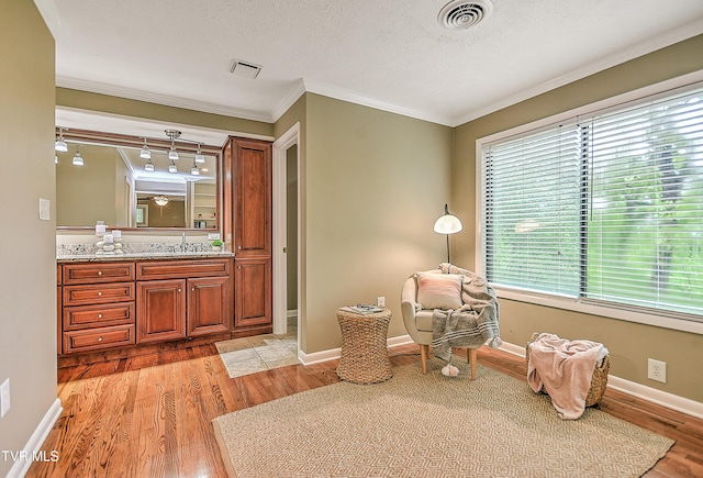 living area with ornamental molding, light wood-style floors, visible vents, and baseboards