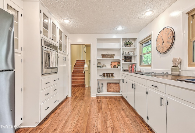 kitchen featuring white cabinetry, light wood-style floors, appliances with stainless steel finishes, and a textured ceiling