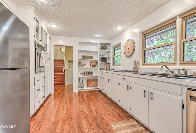 kitchen with a sink, stainless steel appliances, a textured ceiling, white cabinetry, and light wood-style floors