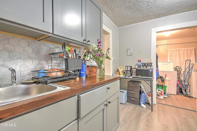 921 E Sevier Ave, Kingsport, TN 37660 - kitchen with a textured ceiling, stainless steel microwave, a sink, decorative backsplash, and light wood-type flooring