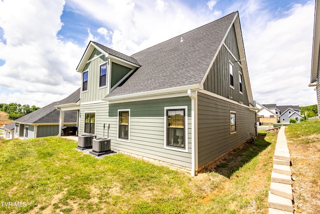 rear view of house featuring board and batten siding, roof with shingles, a lawn, and cooling unit