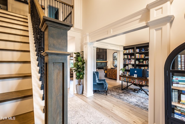 foyer entrance with wood finished floors, stairs, ornate columns, and a towering ceiling