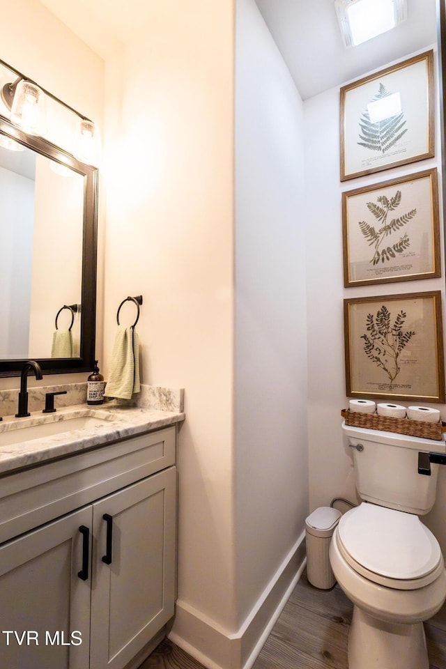 bathroom with baseboards, toilet, wood finished floors, and vanity