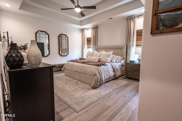 bedroom featuring light wood-style flooring, a raised ceiling, recessed lighting, and ceiling fan