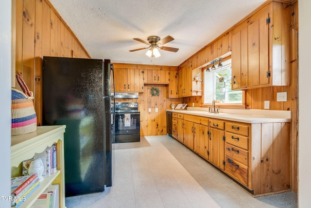 kitchen featuring ceiling fan, wood walls, a sink, and black appliances