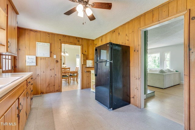 kitchen featuring freestanding refrigerator, a textured ceiling, a ceiling fan, and wooden walls