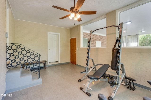 workout room featuring a textured ceiling, ceiling fan, and brick wall
