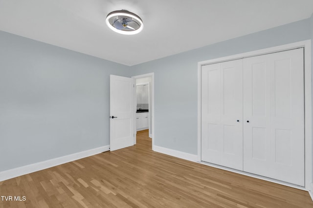 unfurnished bedroom featuring light wood finished floors, baseboards, and a closet