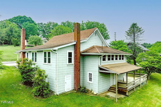back of property with roof with shingles, a wooden deck, a chimney, and a lawn