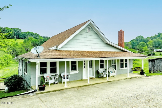 back of house featuring a porch, a shingled roof, and a chimney