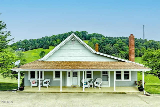 back of house featuring covered porch, roof with shingles, and a chimney