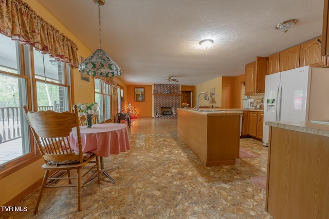 kitchen featuring a fireplace, light countertops, white fridge with ice dispenser, and a healthy amount of sunlight