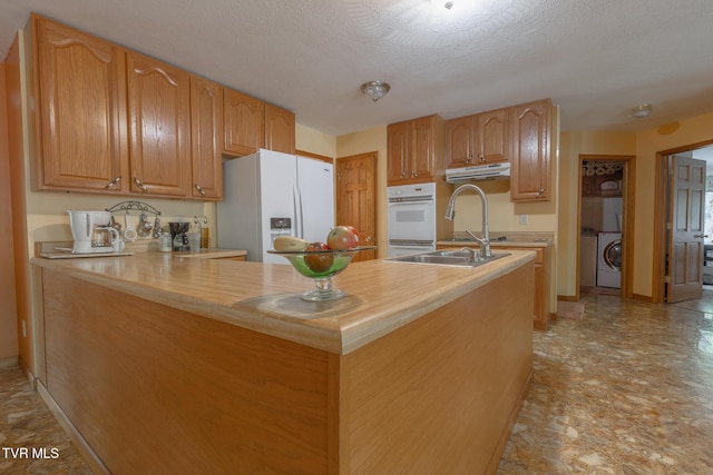 kitchen featuring a peninsula, white appliances, washer / dryer, under cabinet range hood, and light countertops