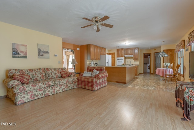 living area with washer / dryer, light wood finished floors, and ceiling fan