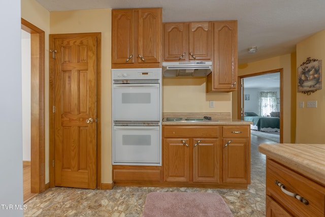 kitchen featuring stovetop, light countertops, double oven, and under cabinet range hood