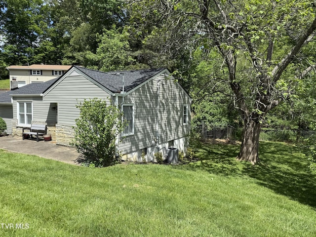 view of side of home with a yard, a patio area, and roof with shingles
