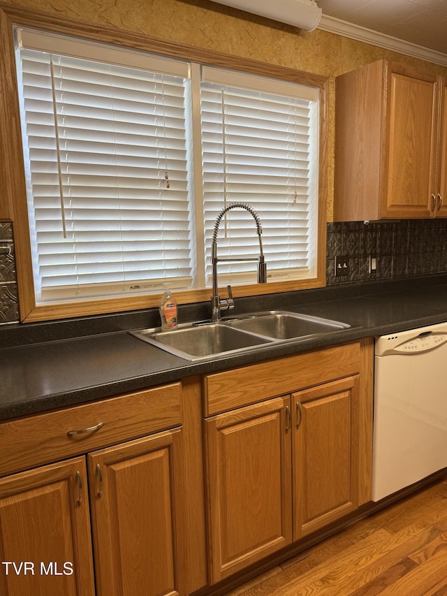 kitchen with white dishwasher, dark countertops, ornamental molding, and a sink