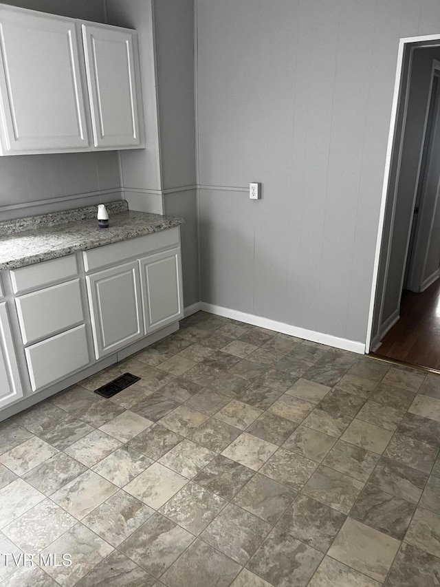 interior space featuring light stone counters, stone finish floor, visible vents, white cabinets, and baseboards