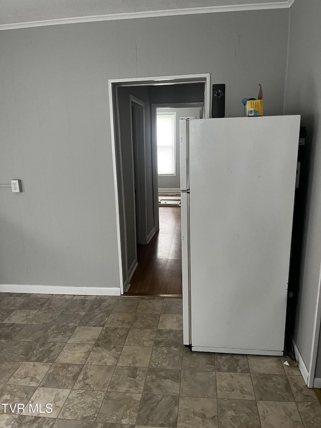 kitchen with freestanding refrigerator, baseboards, crown molding, and stone finish floor