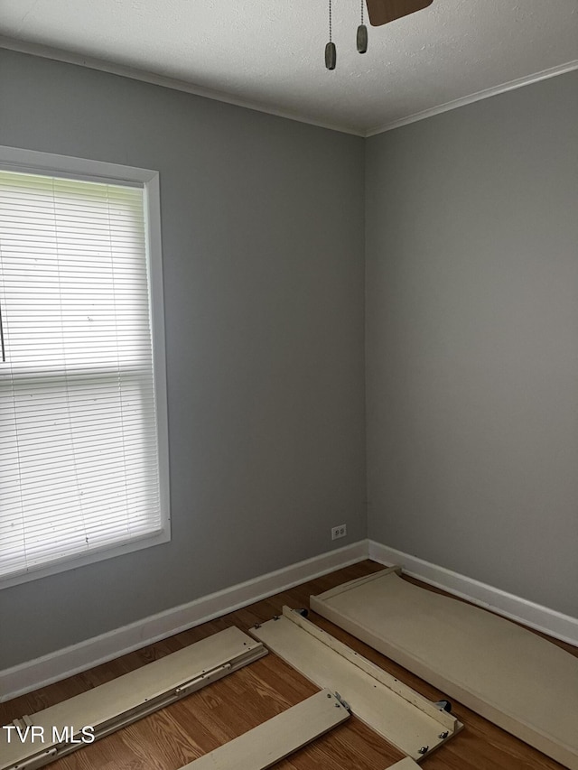 spare room featuring ornamental molding, baseboards, and wood finished floors