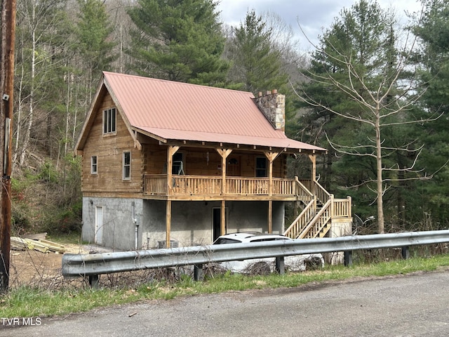 back of house with metal roof, stairs, a forest view, and a chimney