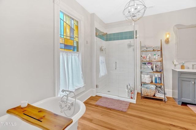 full bathroom with a stall shower, a notable chandelier, vanity, a soaking tub, and wood finished floors