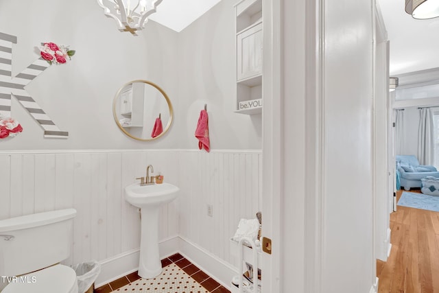 bathroom with a notable chandelier, toilet, a sink, tile patterned flooring, and a wainscoted wall