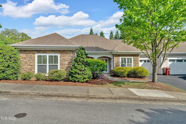 ranch-style house with a shingled roof, stone siding, and aphalt driveway