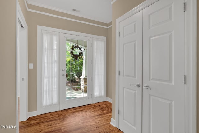 entryway with wood finished floors, visible vents, baseboards, and ornamental molding