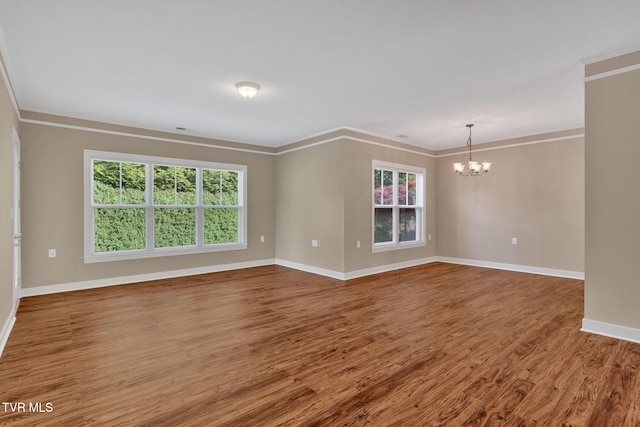 unfurnished room with wood finished floors, baseboards, ornamental molding, and a notable chandelier
