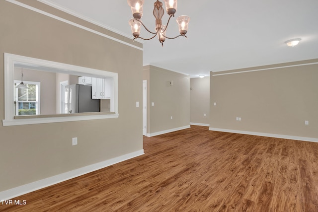unfurnished room with crown molding, baseboards, a notable chandelier, and wood finished floors