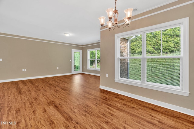 spare room featuring a chandelier, ornamental molding, baseboards, and a healthy amount of sunlight