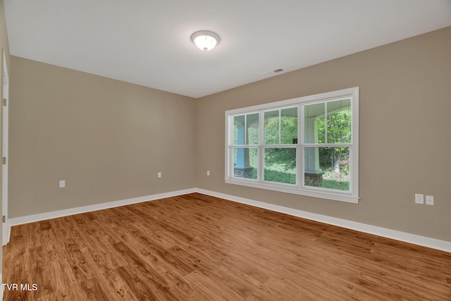 empty room featuring visible vents, wood finished floors, and baseboards