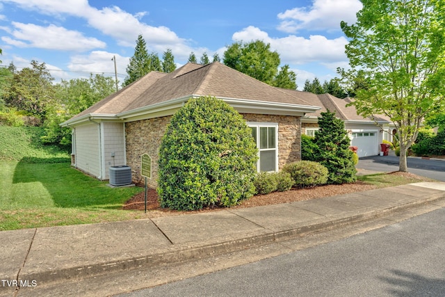 view of side of property with central air condition unit, roof with shingles, stone siding, a yard, and a garage