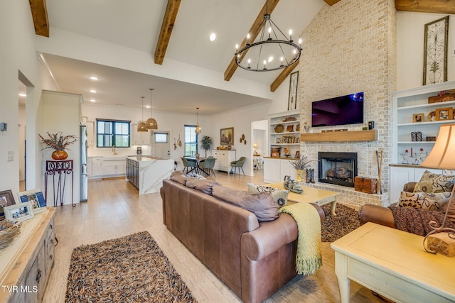 living room featuring a chandelier, light wood finished floors, beam ceiling, a brick fireplace, and recessed lighting