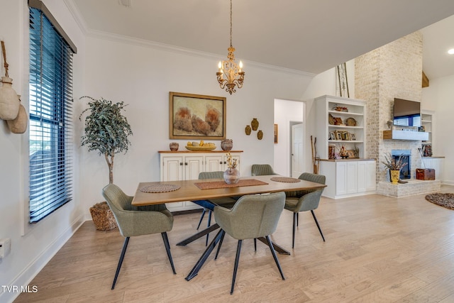 dining area featuring light wood-style flooring, a chandelier, crown molding, a fireplace, and baseboards