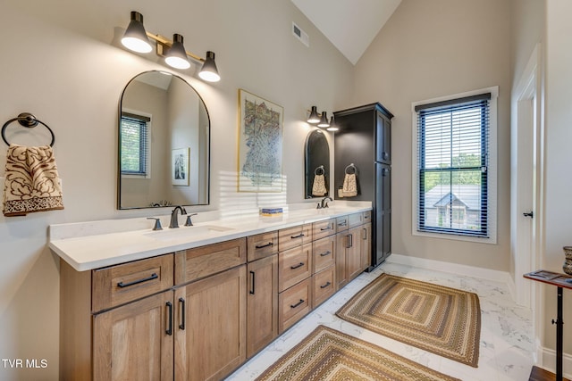 bathroom with marble finish floors, vaulted ceiling, and double vanity