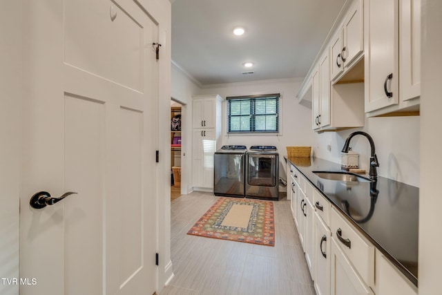 kitchen with a sink, independent washer and dryer, crown molding, dark countertops, and white cabinets