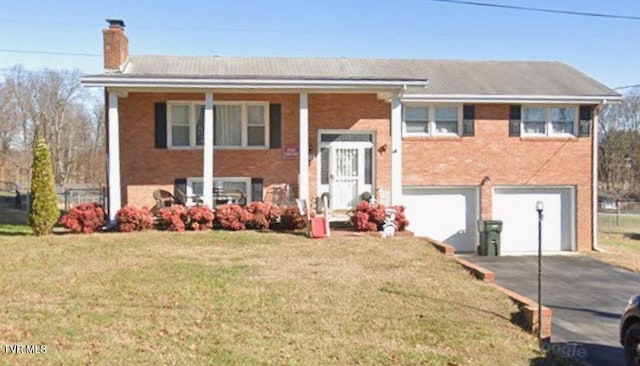 raised ranch featuring concrete driveway, a chimney, an attached garage, a front yard, and brick siding