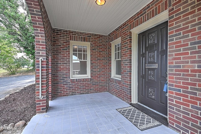 doorway to property featuring a porch and brick siding